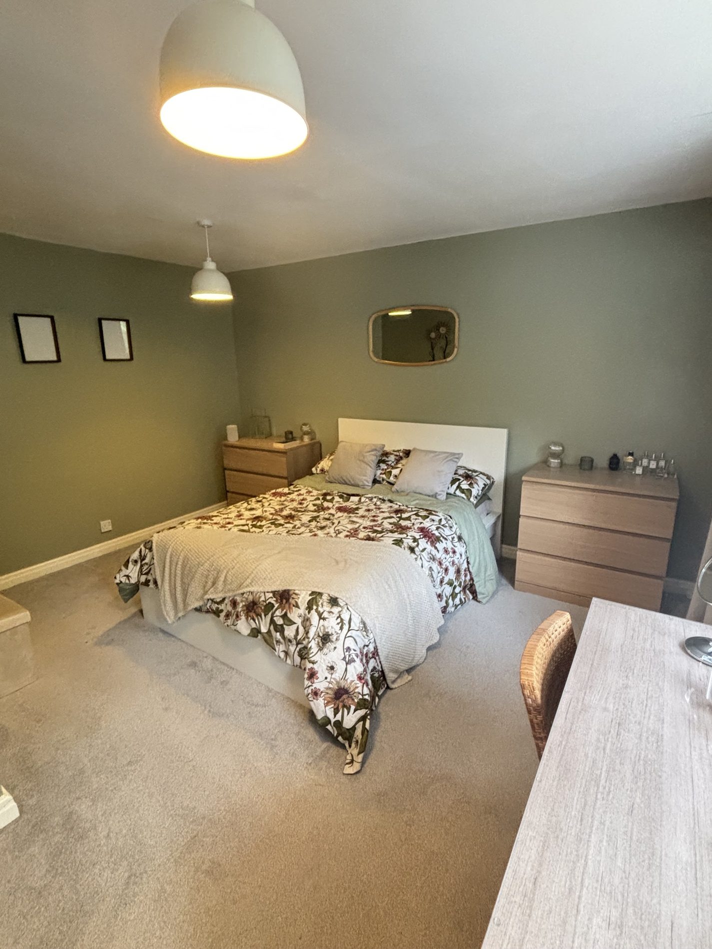 A sage green bedroom with a floral duvet and a gold mirror
