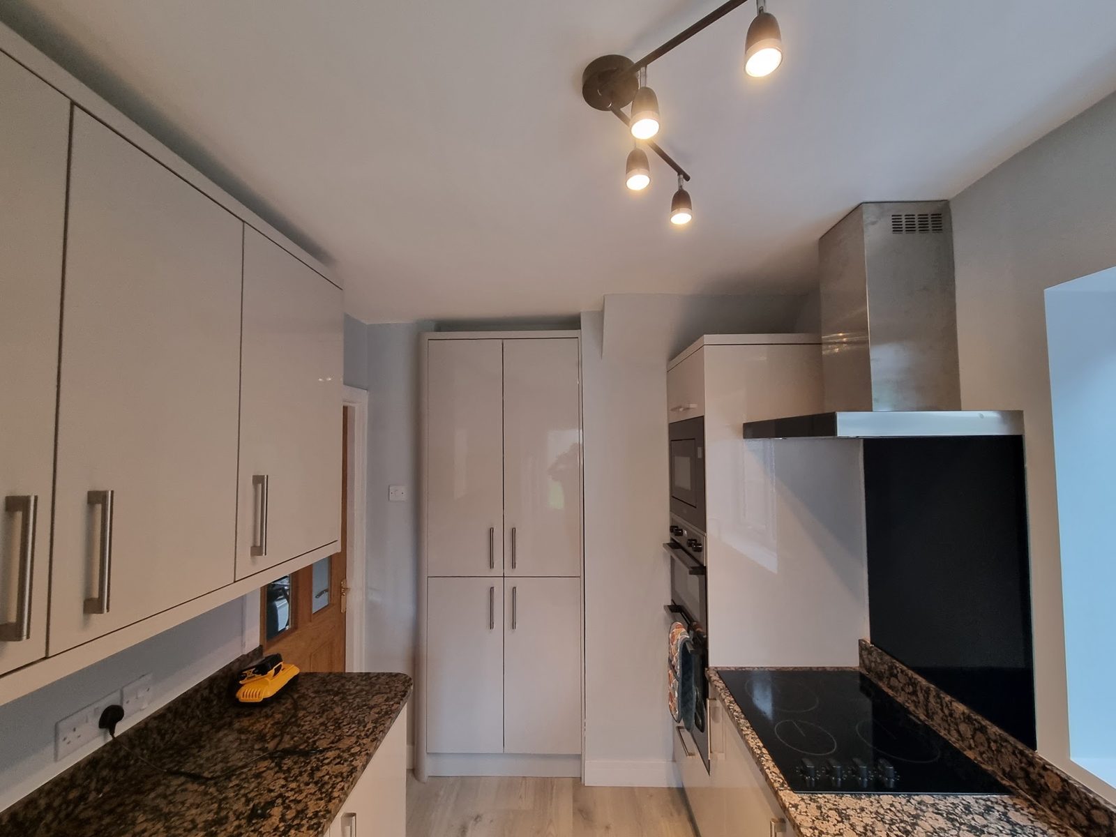 A kitchen with grey cabinets, a black hob and track lights