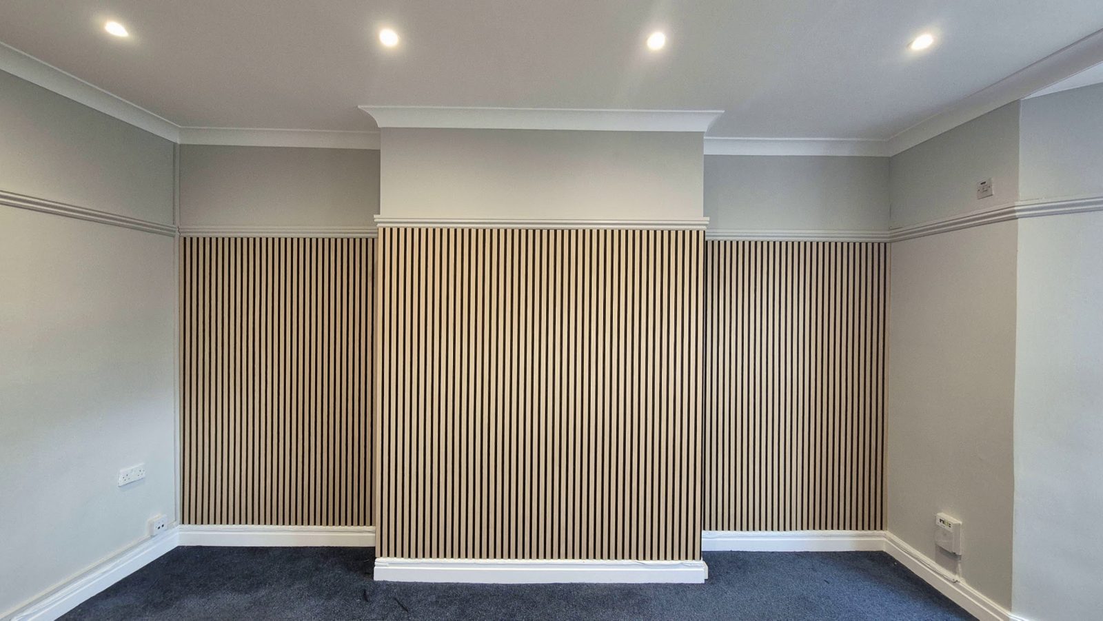 A room with a slatted oak feature wall behind recessed lights
