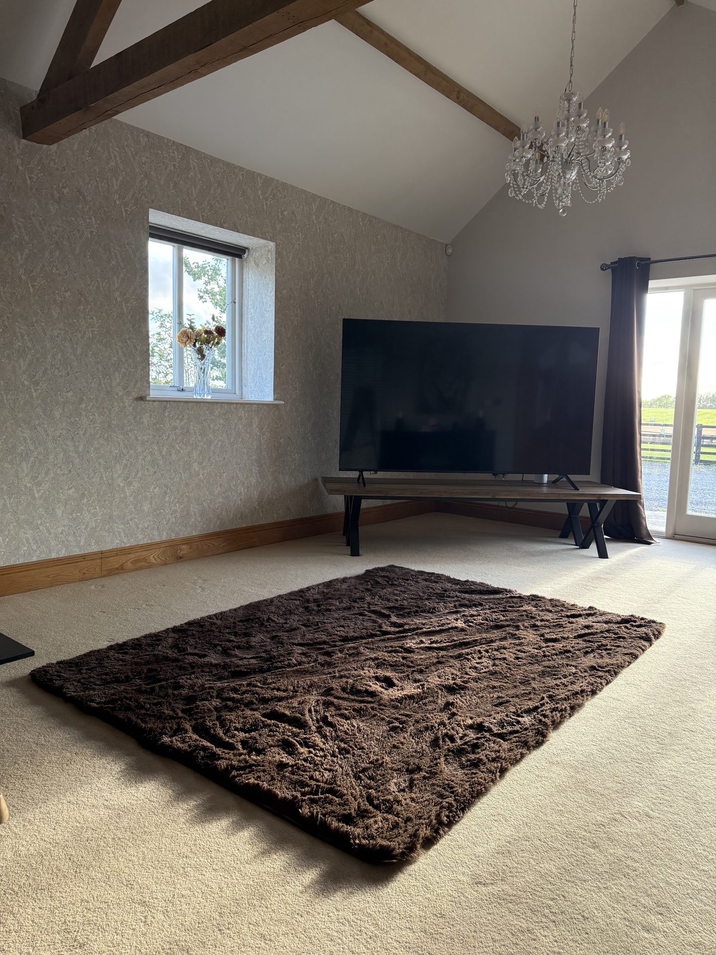 A large living room under a beamed ceiling with a damask feature wall and a crystal chandelier